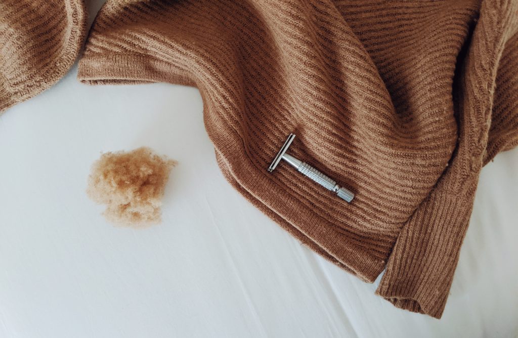A safety razor sitting on a recently de-pilled ochre sweater, with a ball of fuzz on the side